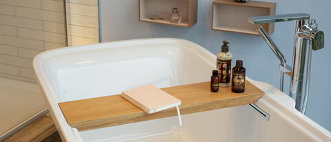 Badewannen-Tablet mit Buch und Pflegeprodukten