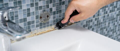 Schimmelige Badezimmerfuge wird mit Cuttermesser ausgeschnitten