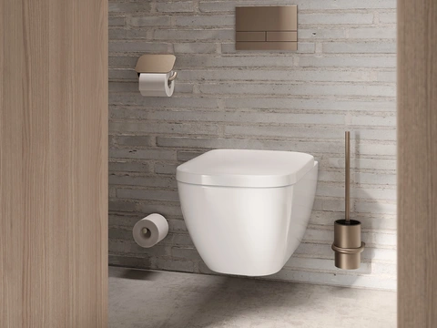 Modernes Badezimmer mit wandhängender weißer Toilette vor heller Backsteinwand, goldfarbenem Spülkasten, passendem Toilettenpapierhalter und WC-Bürste./ HEWI/ S 480