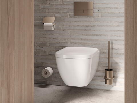 Modernes Badezimmer mit wandhängender weißer Toilette vor heller Backsteinwand, goldfarbenem Spülkasten, passendem Toilettenpapierhalter und WC-Bürste./ HEWI/ S 480