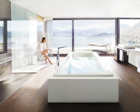 Frau sitzt in einem großen Badezimmer vor einer Fensterfront und entspannt