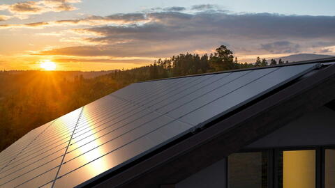 Eine Photovoltaikanlage auf dem Fach. Im Hintergrund geht die Sonne auf