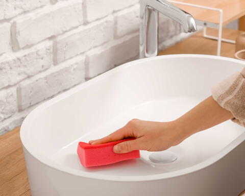 Frau wischt mit rotem Reinigungsschwamm ein Waschbecken aus