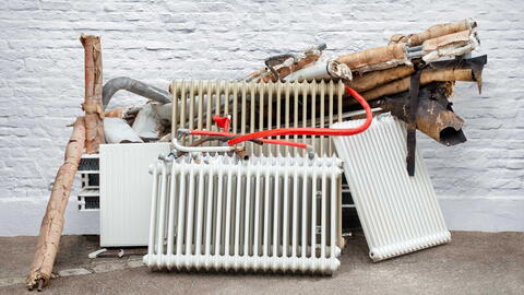 Eine alte Heizungsanlage mit alten Heizkörpern liegt herausgerissen vor einer Hauswand