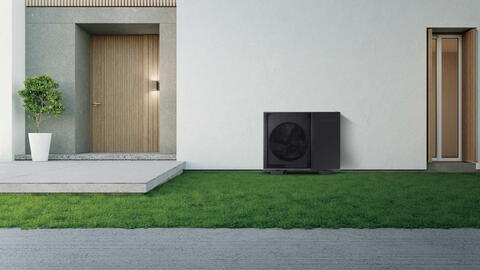 Eine schwarze Wärmepumpe steht vor einer modernen Hausfassade