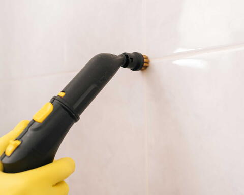 Hand hält elektrische Reinigungsbürste gegen Fliesen