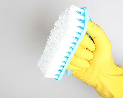Hand mit gelbem Gummihandschuh hält eine blaue Reinigungsbürste