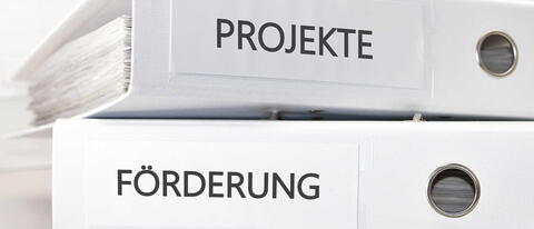 Zwei weiße Ordner liegen aufeinander, jeweils beschriftet mit "Projekte" und "Förderung"